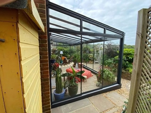 A greenhouse with sliding glass doors and a table and chairs inside of it.