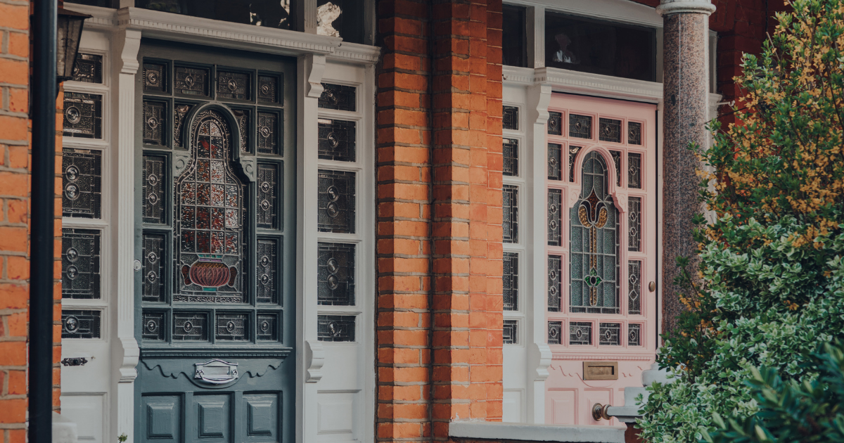 Two ornate doors with detailed glass panels, one dark blue and one pale pink, set in a brick exterior.