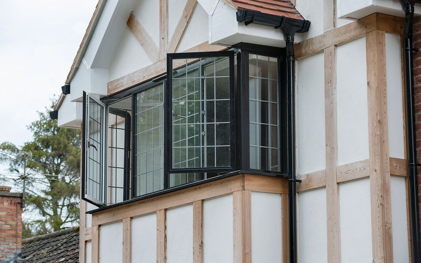 A Tudor-style house exterior with white plaster, exposed timber framing, and open Heritage black-framed casement windows.