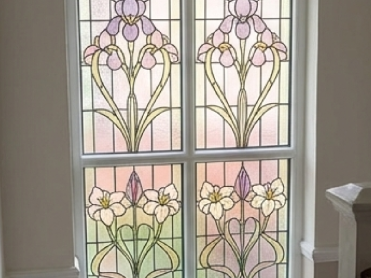 A stained glass window featuring four panes with symmetrical floral designs in purple, white, and yellow on a grid frame.