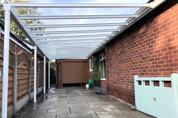 A carport with a glass roof is attached to a brick house.