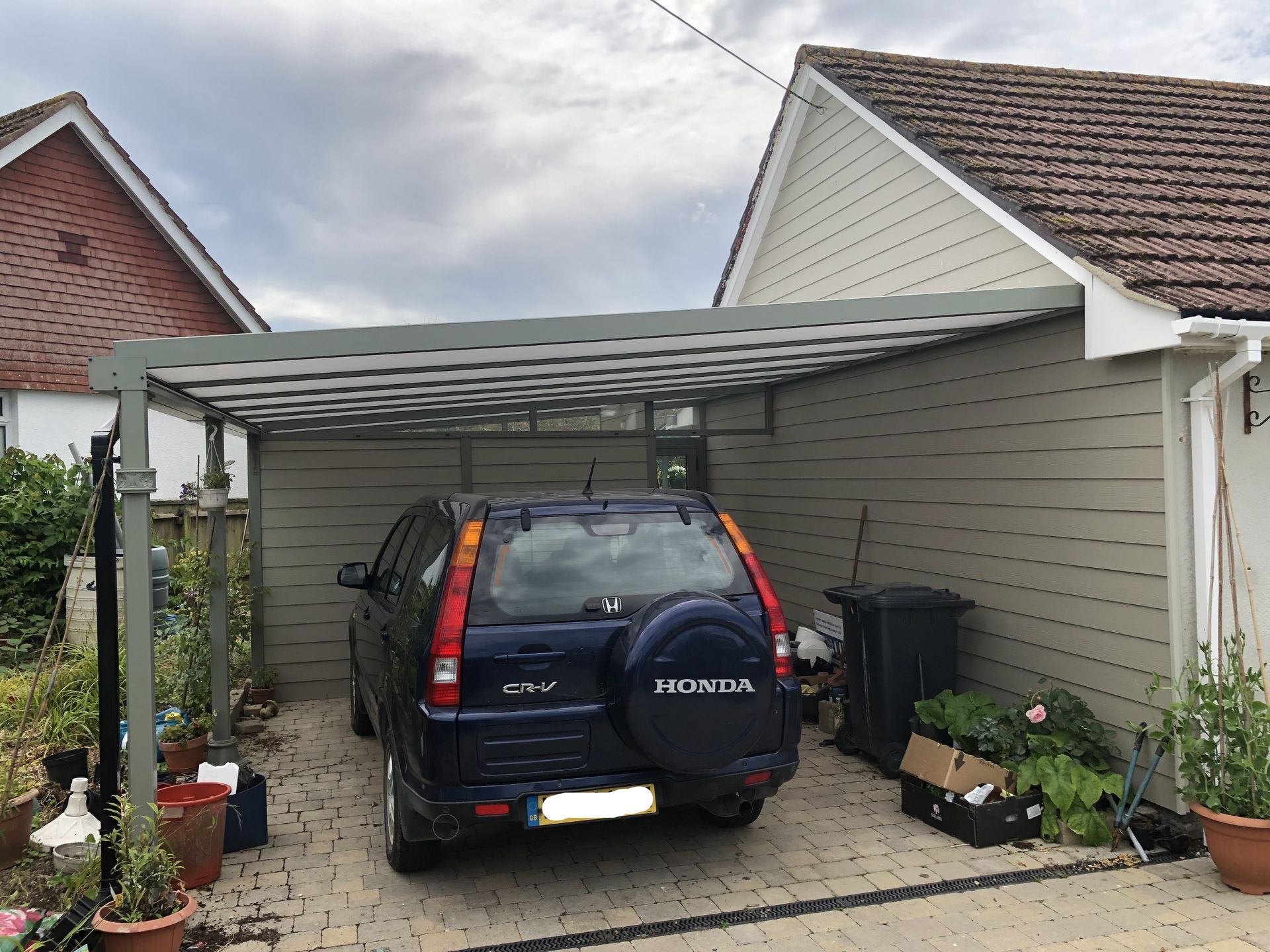 A car is parked under a canopy in front of a house.