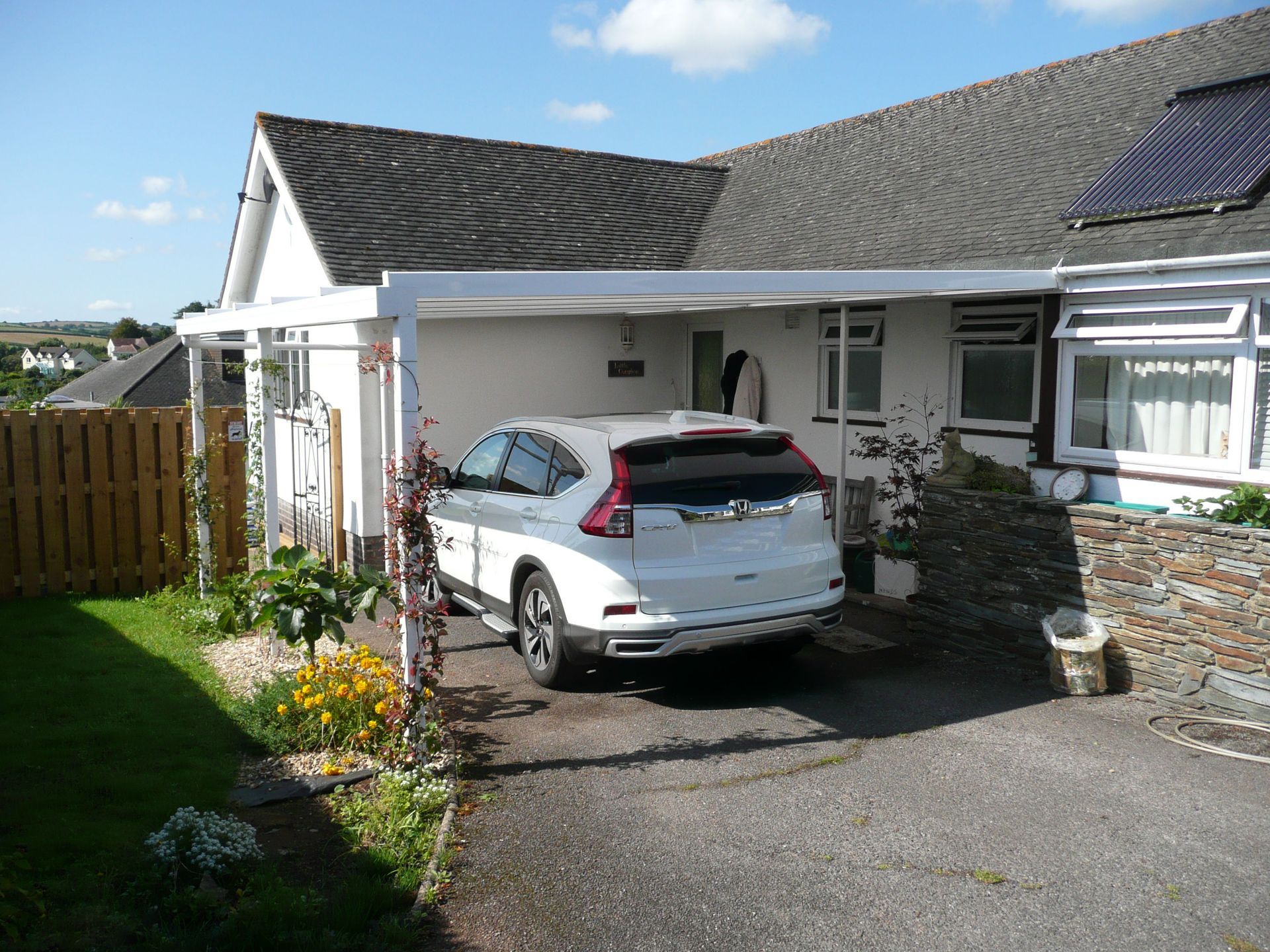 A white car is parked under a canopy in front of a house.
