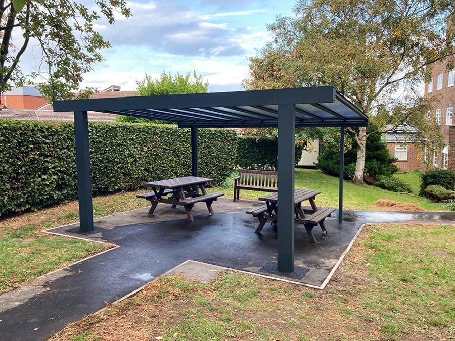 A picnic area with tables and benches under a pergola in a park.