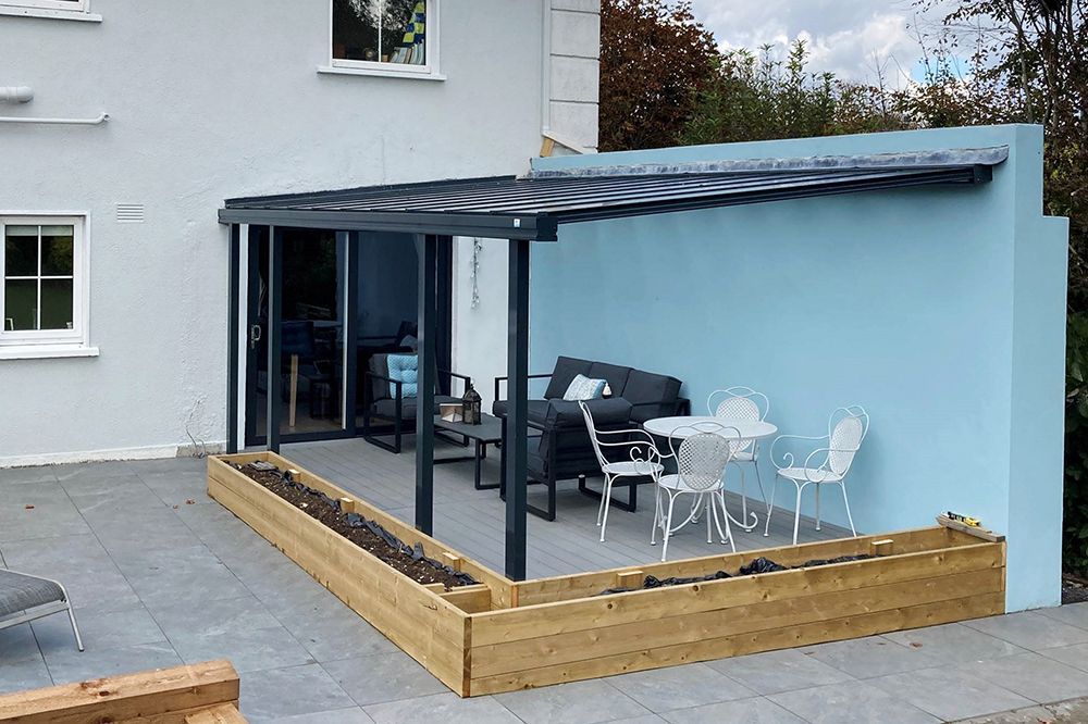 A patio with a couch , table and chairs in front of a house.