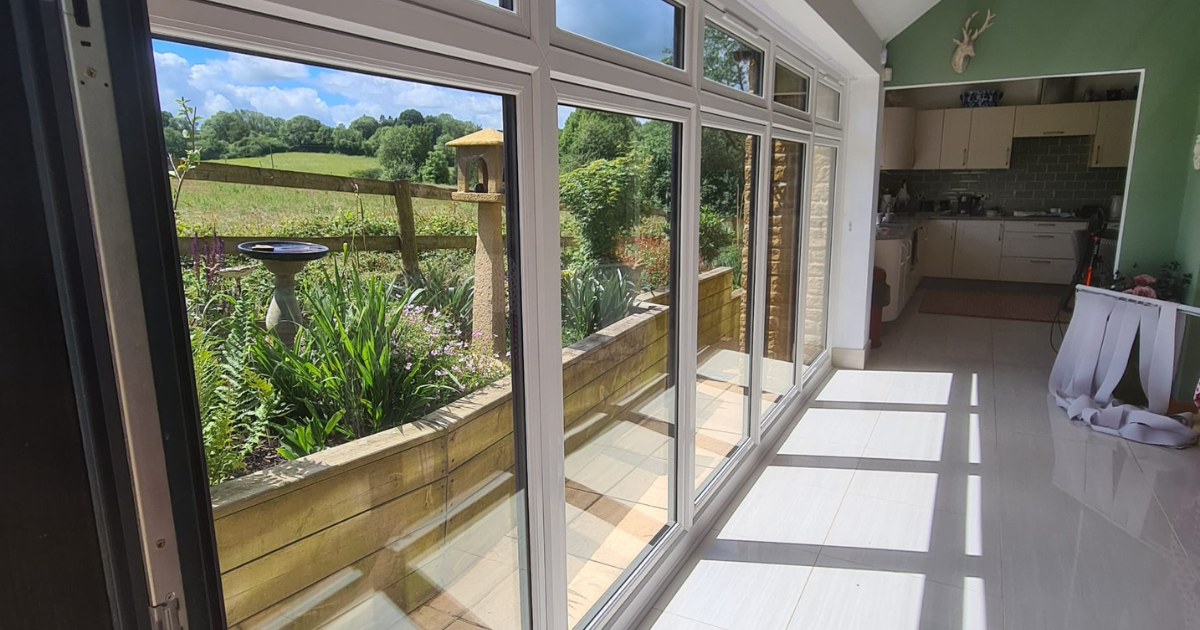 Bright sunlit lounge with large glass windows overlooking a garden and fields, installed in Moreton in Marsh
