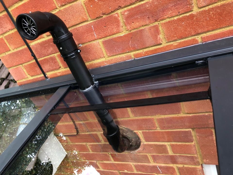 A black pipe is hanging from the side of a brick building.