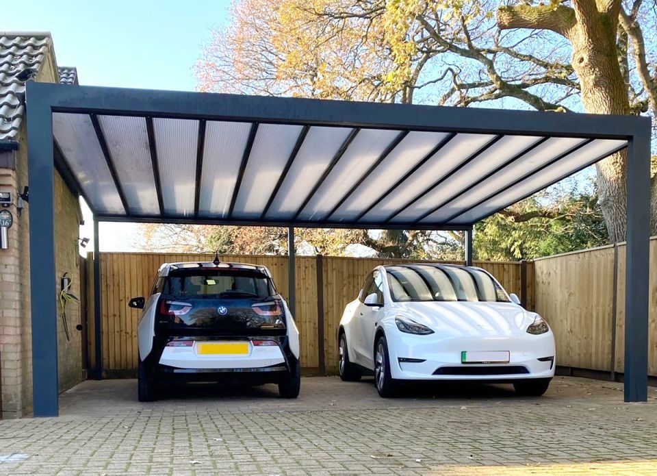 Two electric cars are parked under a canopy in a driveway.