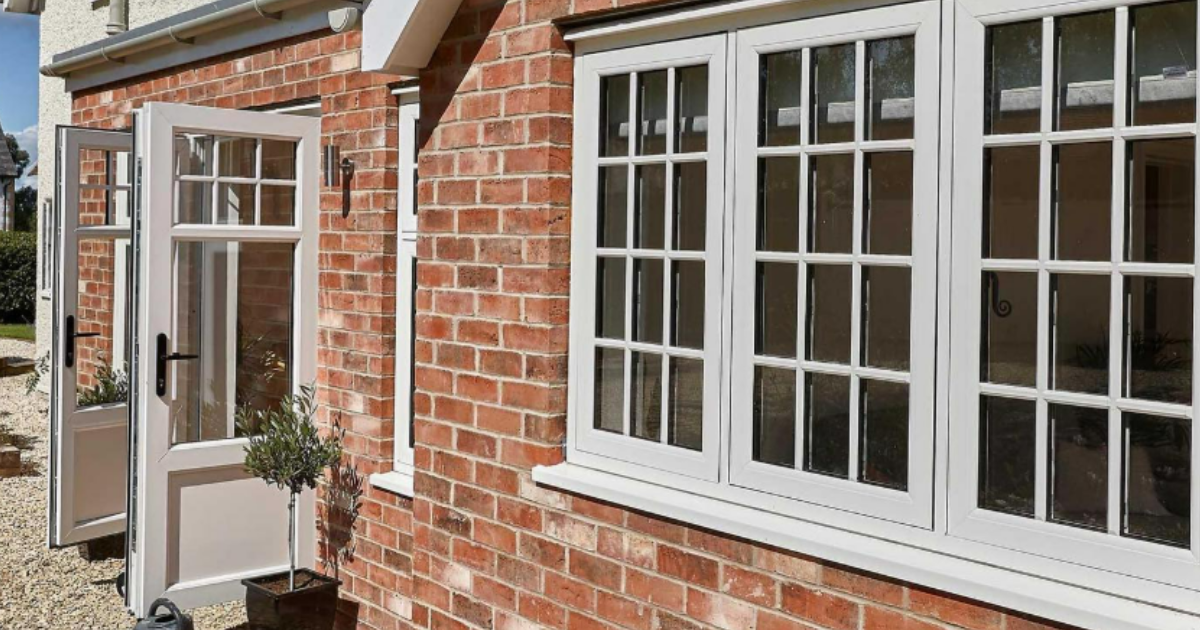A red brick exterior wall featuring a set of open white French doors and a three-pane white grid window installed by Prior Products Stratford-upon-Avon