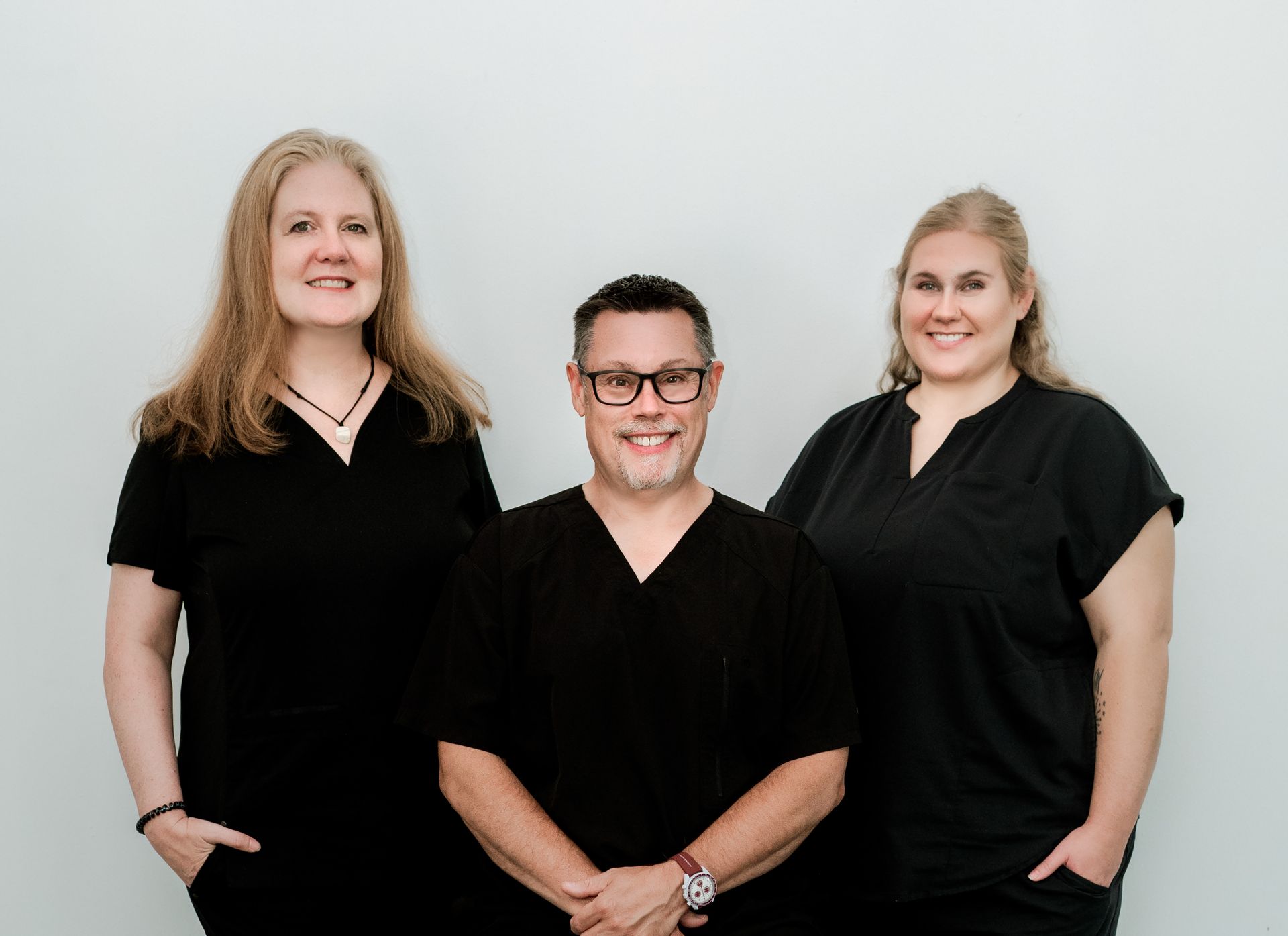 Three healthcare professionals in black scrubs smiling in front of a light wall.