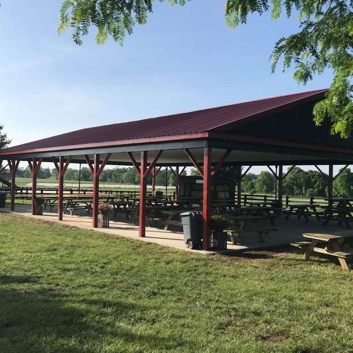 A large, open-air pavilion with a burgundy metal roof, dark wooden support beams, and many picnic tables inside.