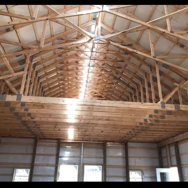 Interior view of a barn or shed showing wooden roof trusses and an open loft level above a framed ground floor.