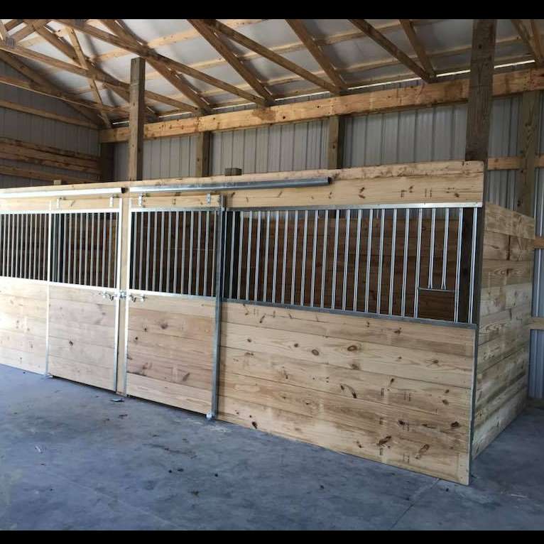Two wooden horse stalls with sliding front doors and metal grate tops inside a barn.