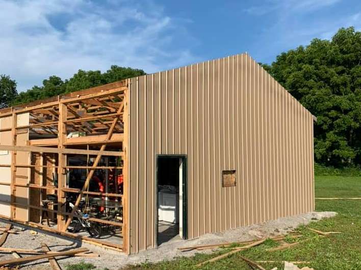 A metal-sided building under construction with exposed wooden framing on the left and a finished exterior on the right.