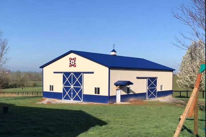 A cream and blue metal barn with double sliding doors and a cupola, situated on a grassy landscape under a clear sky.