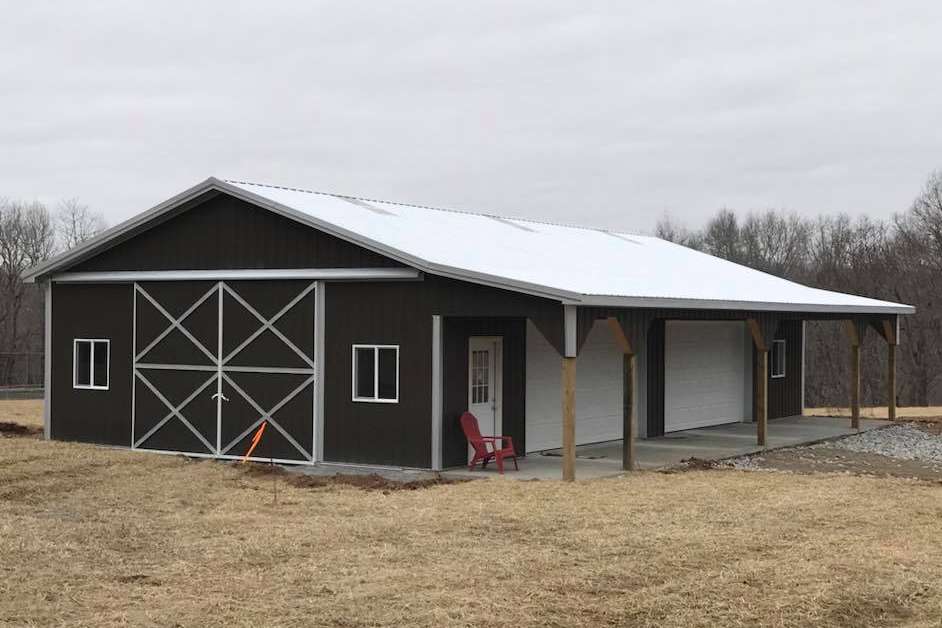 A brown, metal-sided barn with white trim, a gabled roof, sliding double doors, a side entrance, and a covered porch.