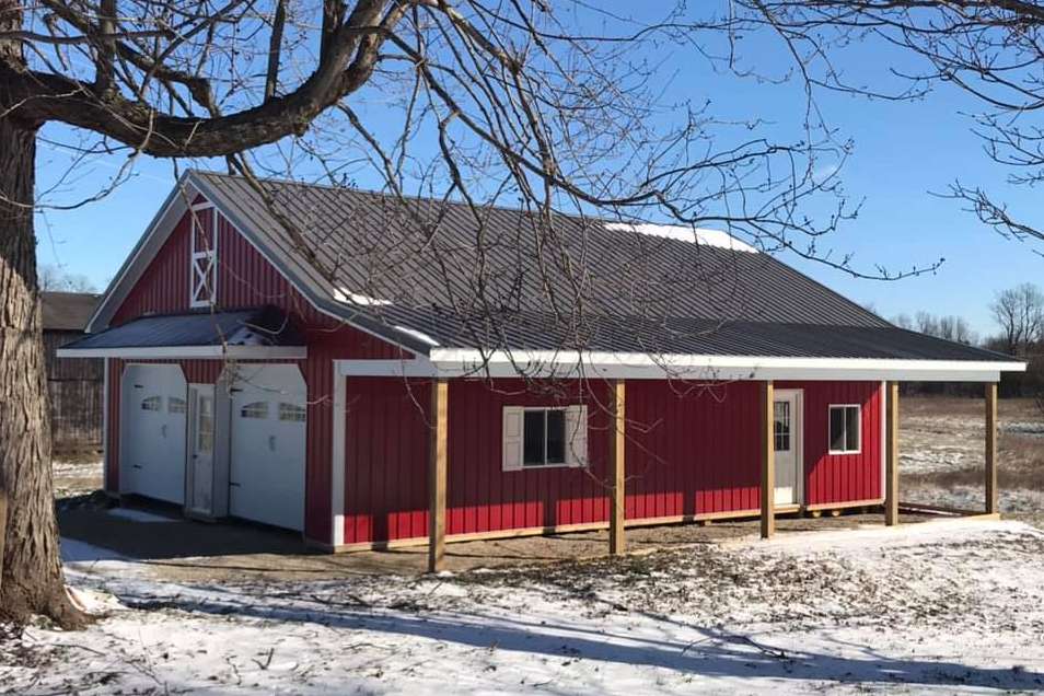 A red barn-style building with white trim, two garage doors, and a covered porch in a snow-covered field.