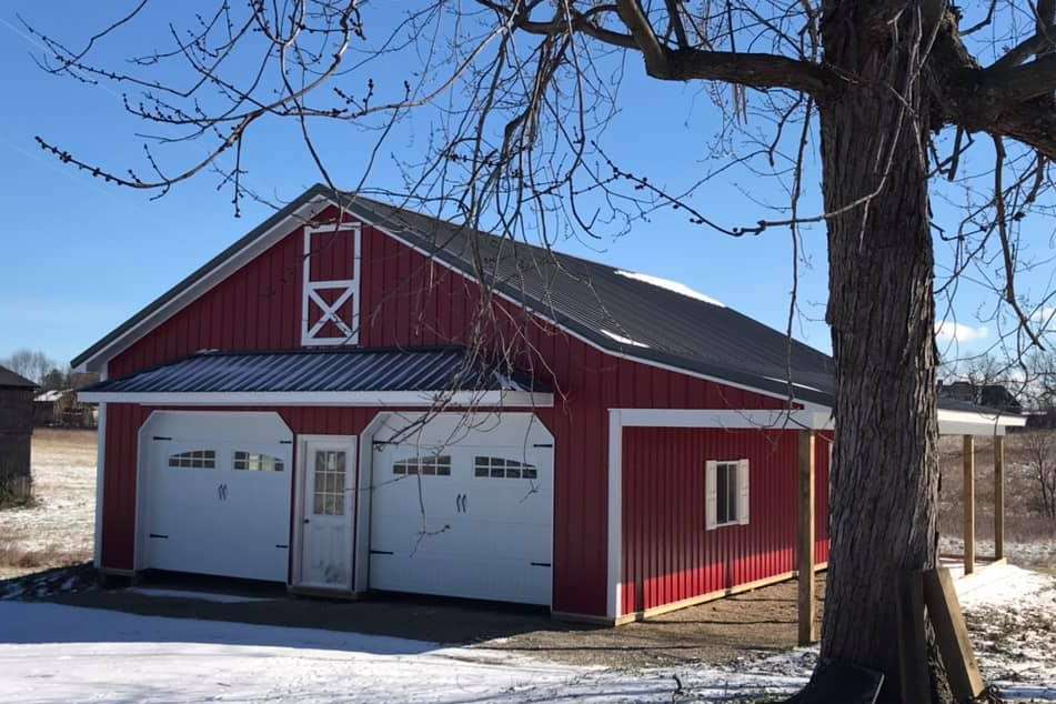 A red barn-style garage with two white doors and a central entrance, situated in a snowy, rural landscape.