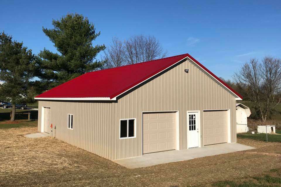 Tan metal garage with a red roof, two garage doors, a side entry door, and windows on a grassy lot under a blue sky.