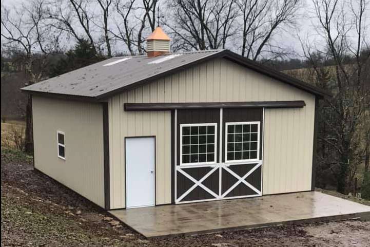 A tan and brown barn-style shed with a sliding door featuring windows, a white side door, and a copper cupola on the roof.