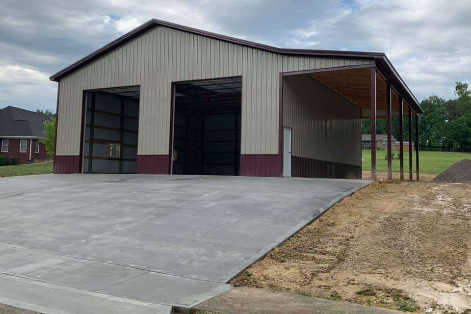 A tan and maroon metal building with two open garage bays and an attached side porch on a concrete slab.