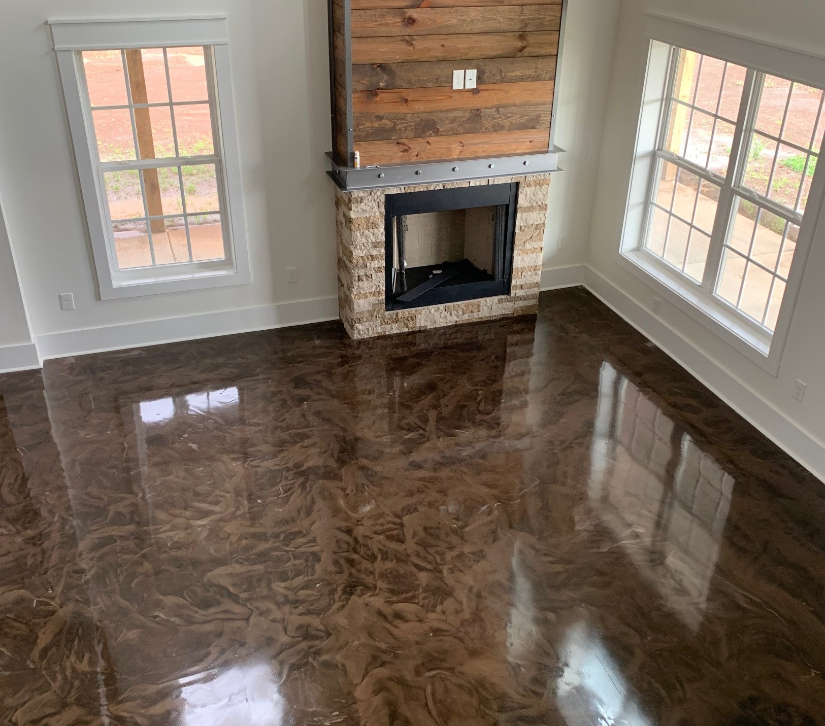 A room with a polished, marbled brown floor, a fireplace with a stone base, wood paneling, and two large windows.