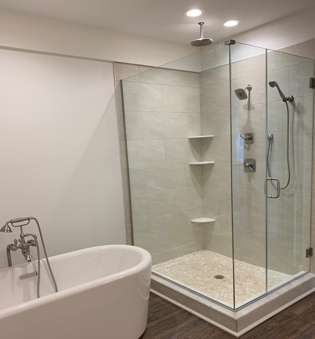 A modern bathroom featuring a white freestanding bathtub next to a glass-enclosed shower with tiled walls and pebble floor.
