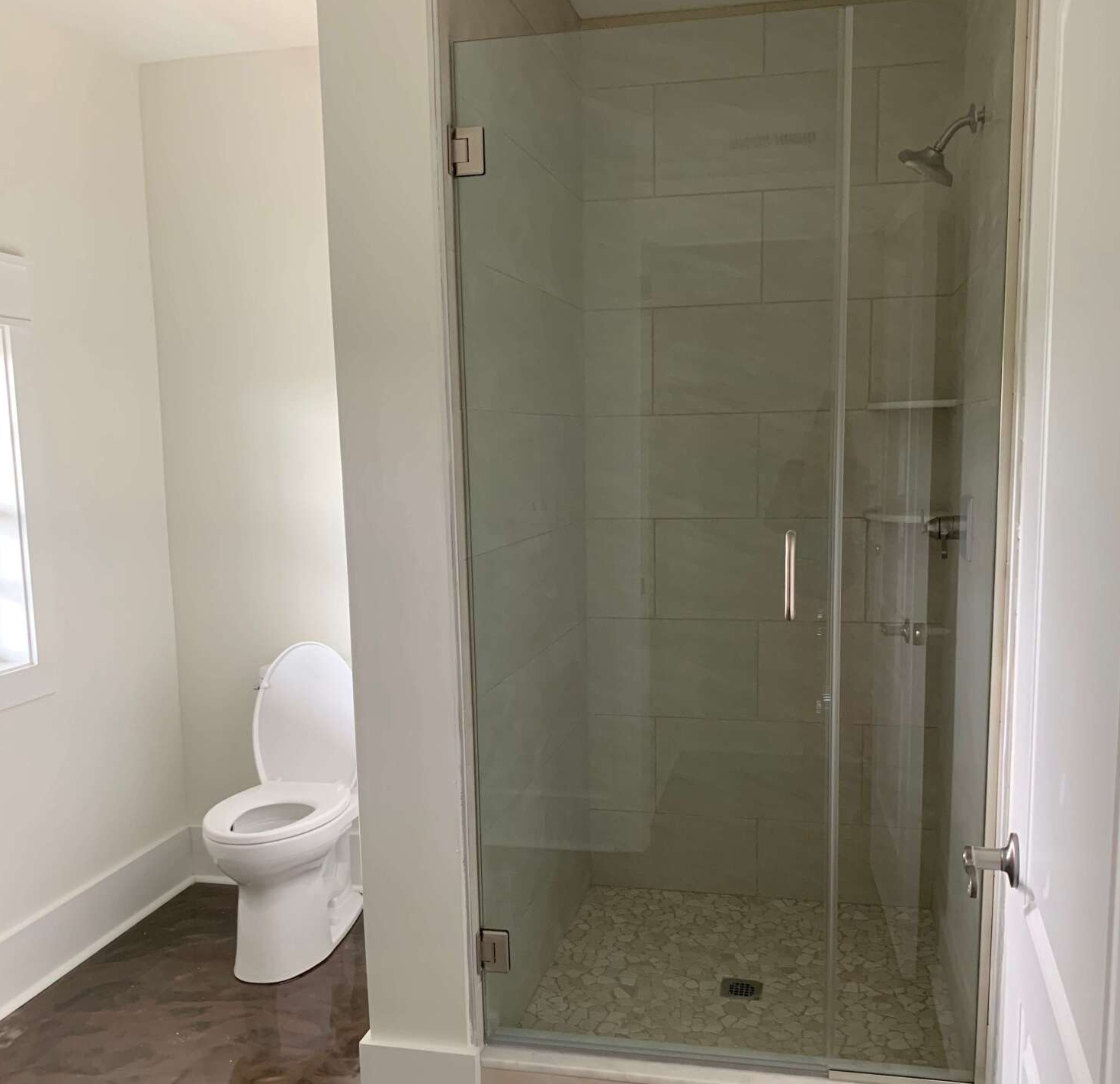 A modern bathroom with white walls, a walk-in shower with glass doors and pebble tile flooring, and a white toilet.