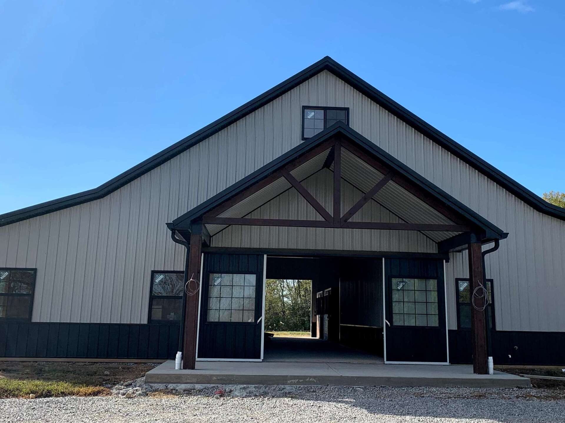 A beige metal building with a dark roof and trim, featuring a central covered porch and open double doors.