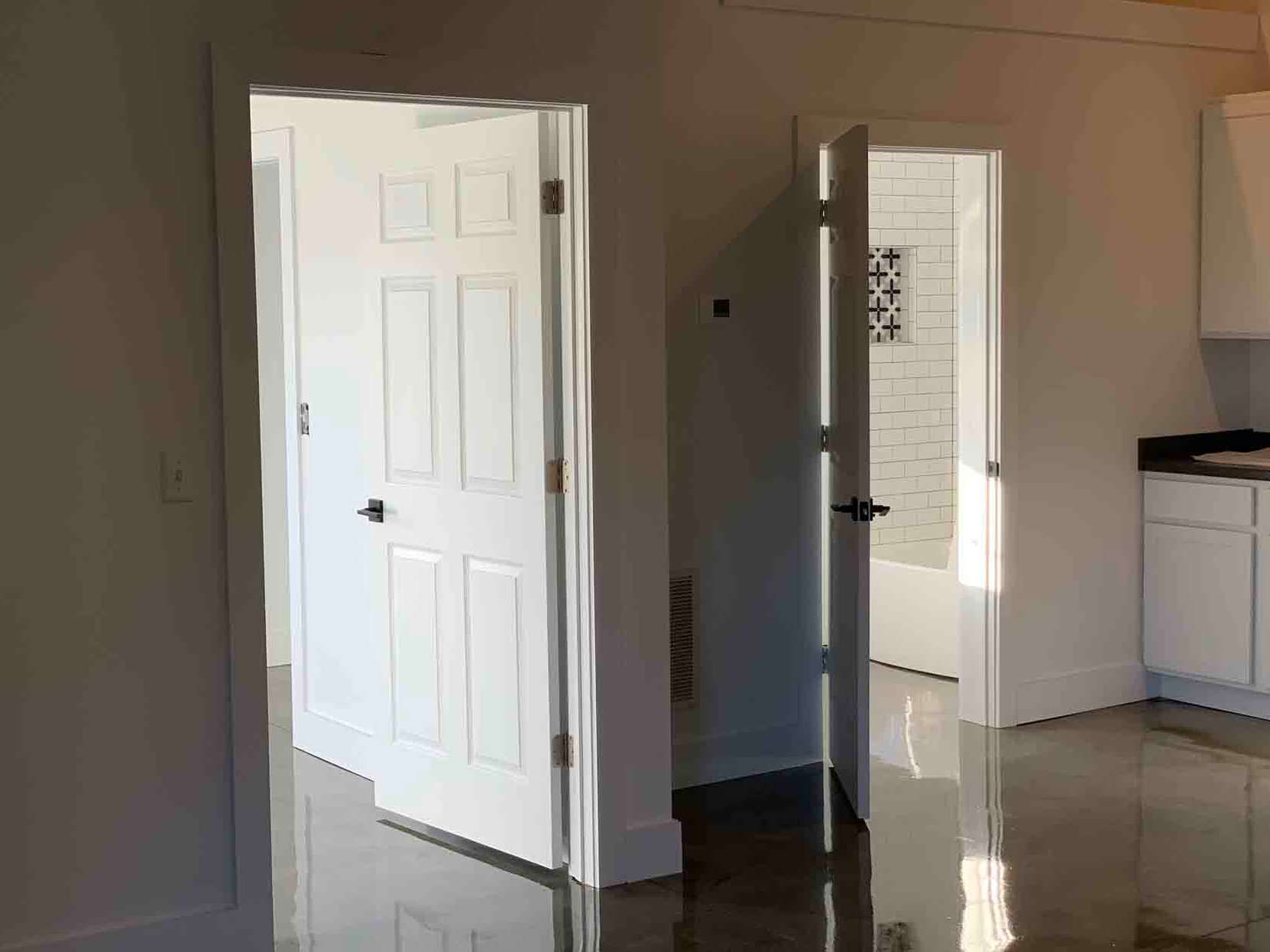 Two white interior doors open into separate rooms with tiled floors in a brightly lit hallway.