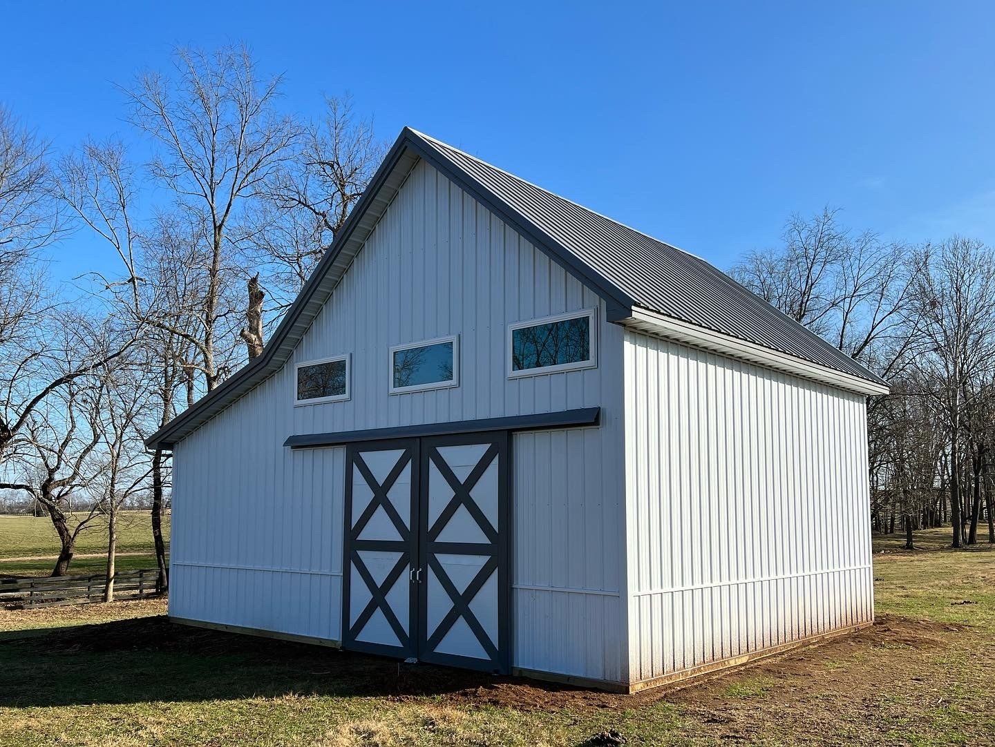 White barn with gray trim, a sliding double door, and three small windows under a pitched roof in a rural setting.