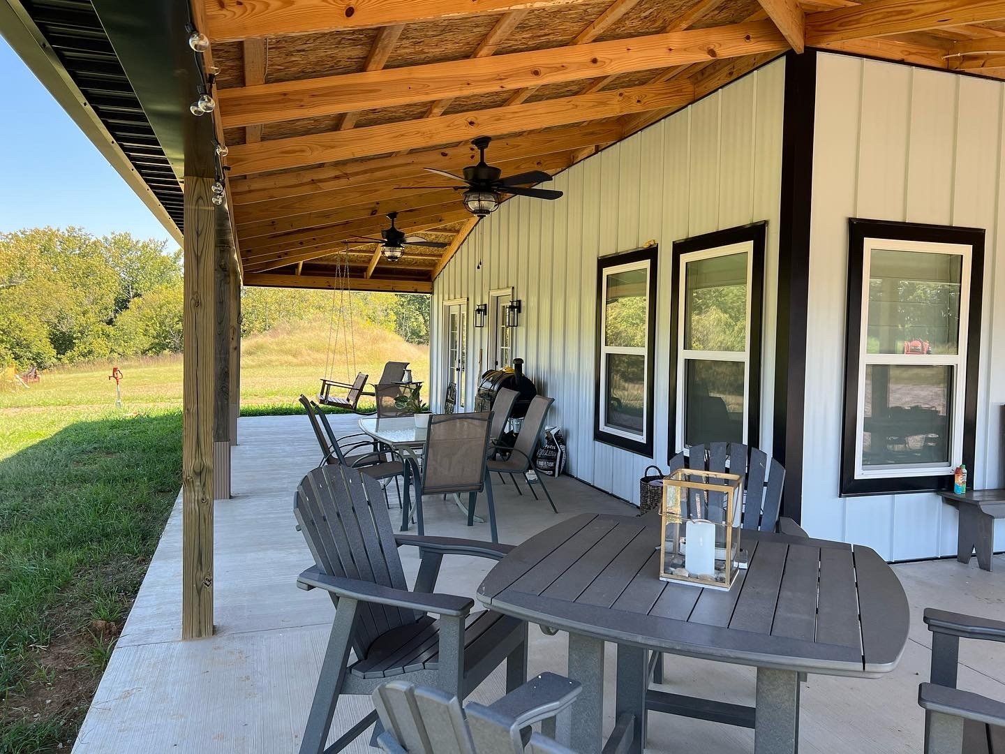 A white modern farmhouse porch with outdoor furniture, ceiling fans, and a view of a grassy field.