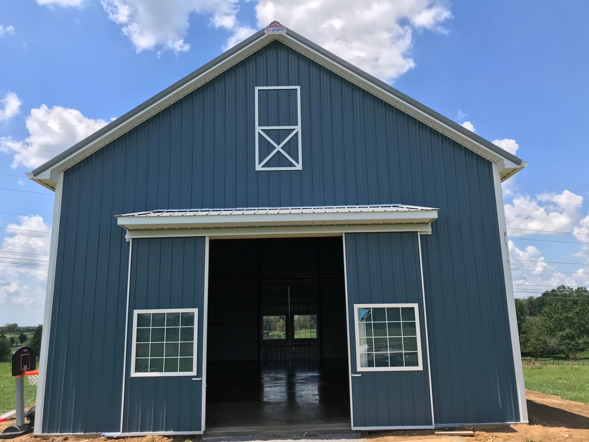 A blue wooden barn with white trim and windows, featuring large open double doors under a blue sky with scattered clouds.