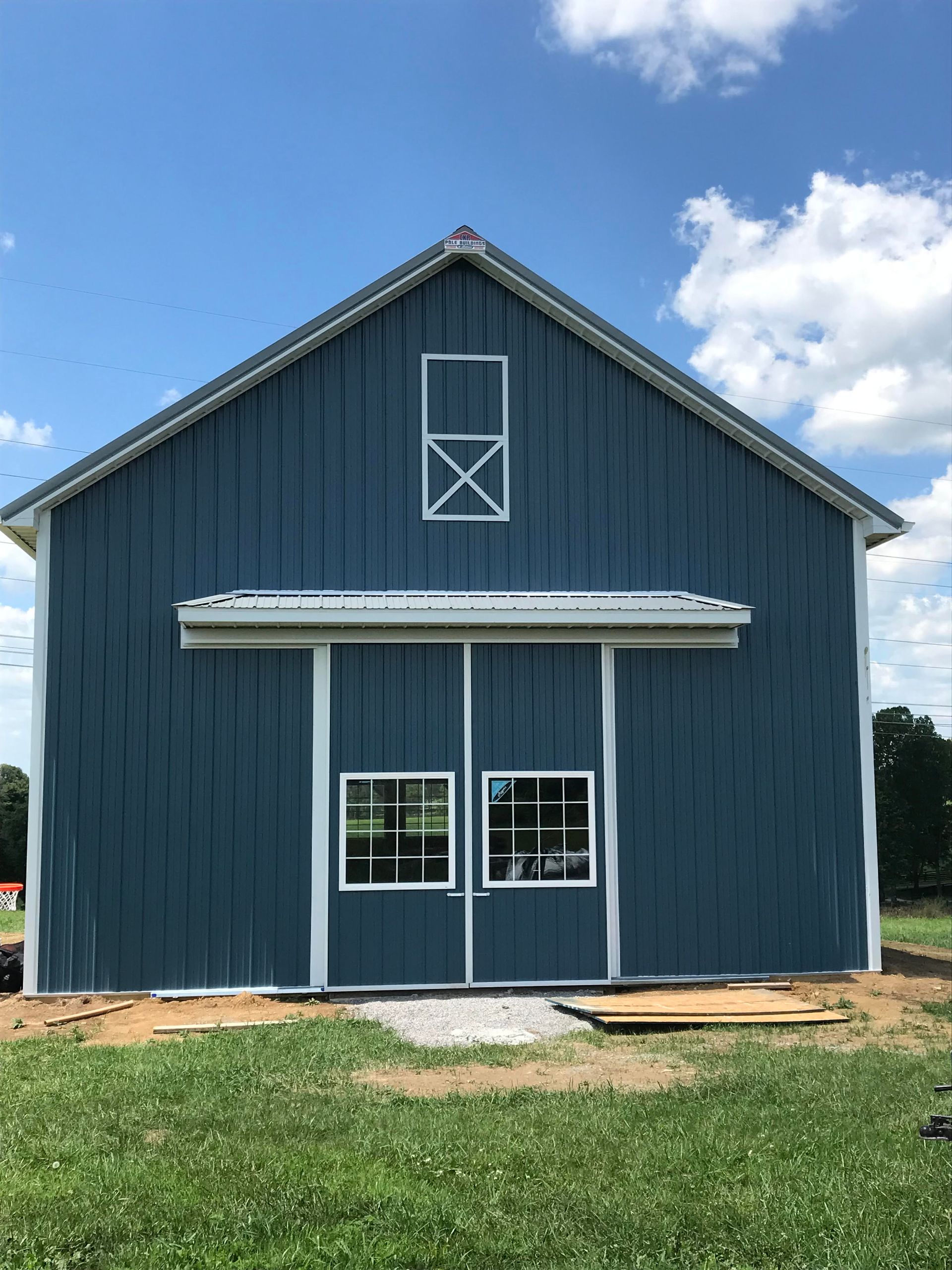 A blue, barn-style building with a white-trimmed door featuring two windows, set against a bright blue, cloudy sky.