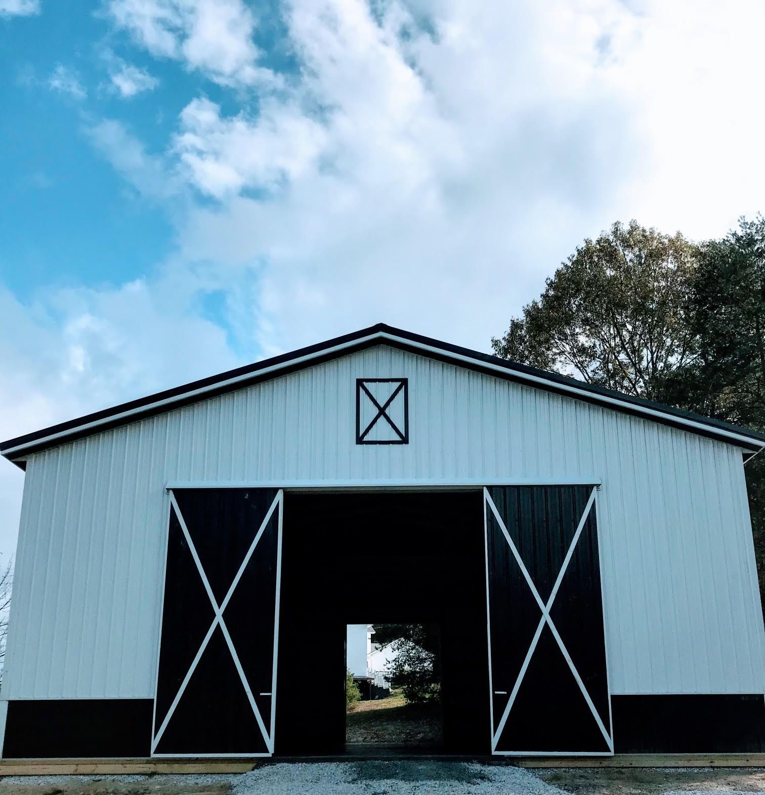 A white barn with black trim and large cross-braced sliding doors stands against a blue sky with soft, wispy clouds.