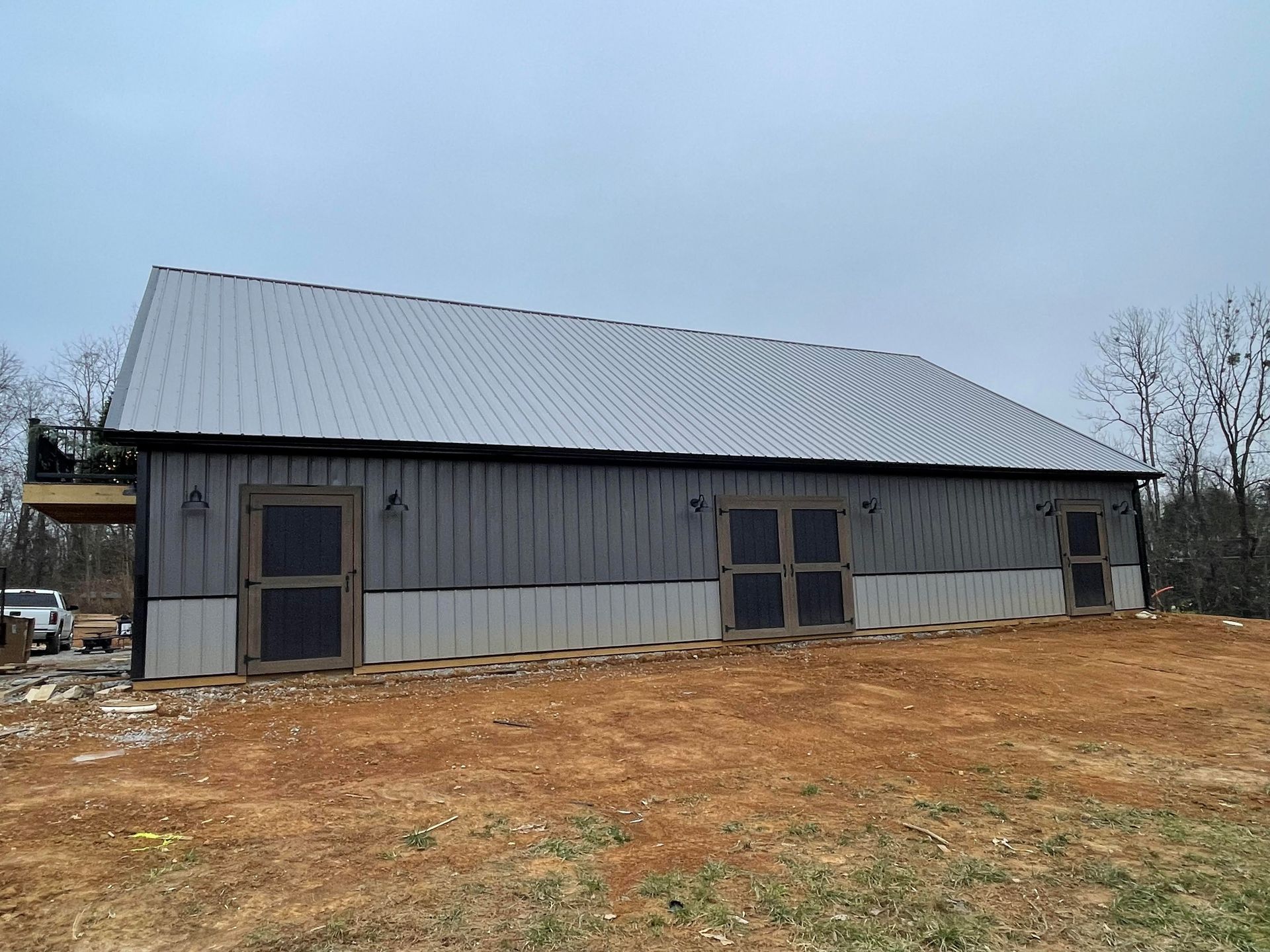 A large, two-tone gray and white metal-sided barn with three sets of double doors, set against a cloudy sky.