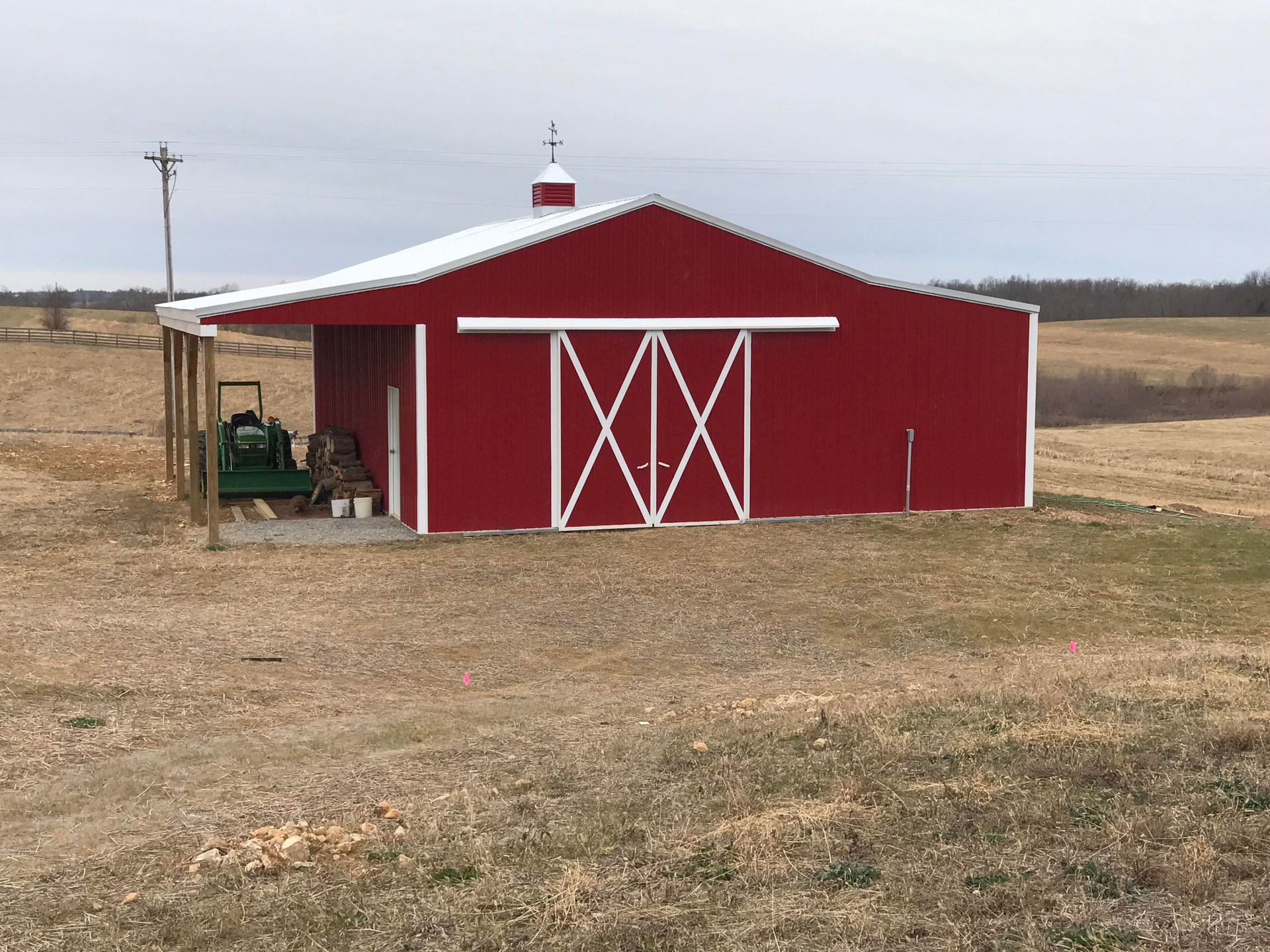 A red barn with white trim and sliding doors sits in a large, dry field under an overcast sky.