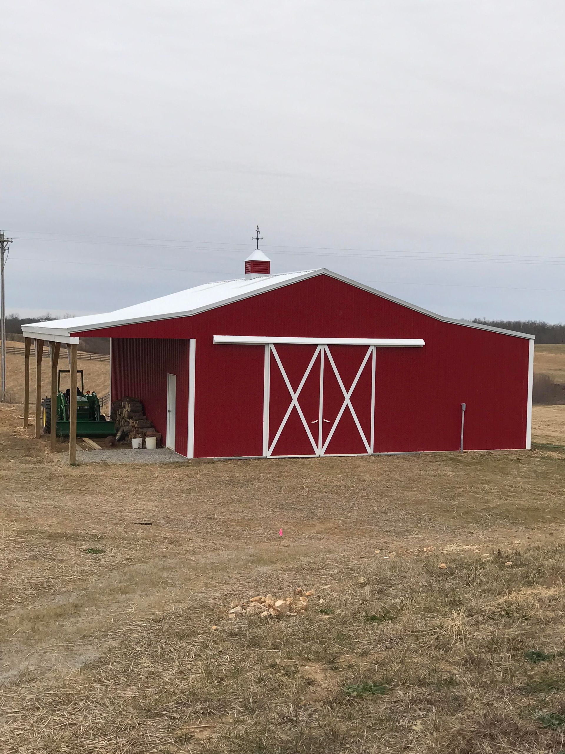 A red barn with a white roof and sliding doors stands in an open field under a cloudy sky.