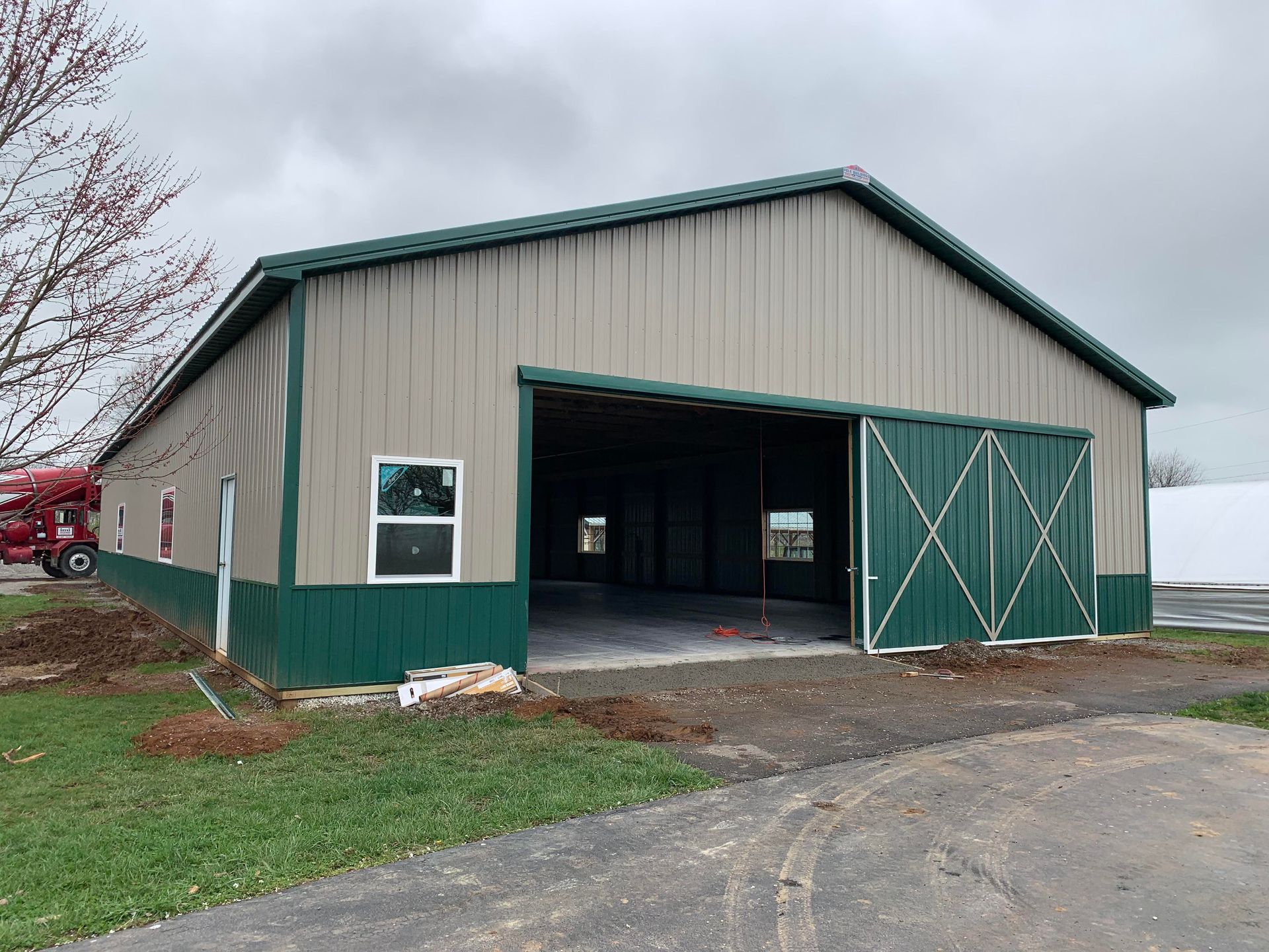 A metal building with tan siding and dark green trim, featuring a large open sliding door and white-framed windows.