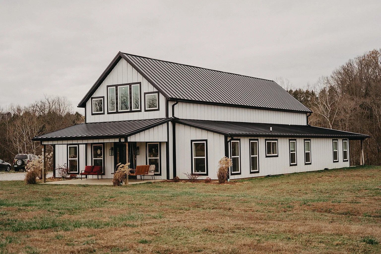 A white farmhouse with a dark metal roof, black window frames, and a wrap-around porch, set in a dry grassy field.