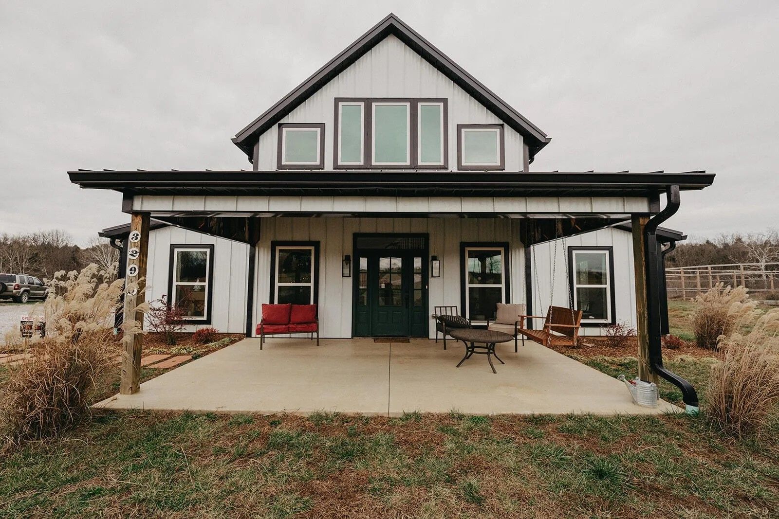 A white farmhouse with a black metal roof, front porch, and symmetrical windows under a cloudy sky.