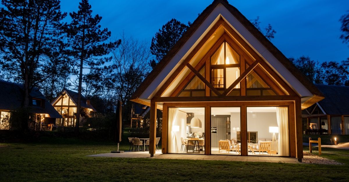 A converted barn with large windows showing a top and bottom floor. It is night, and the interior lights are on.