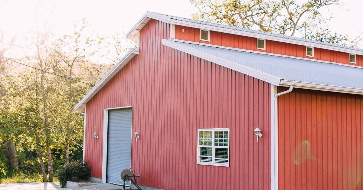 The exterior of a large red barn with a vaulted roof. The side of the barn has a gray roller door and a window.