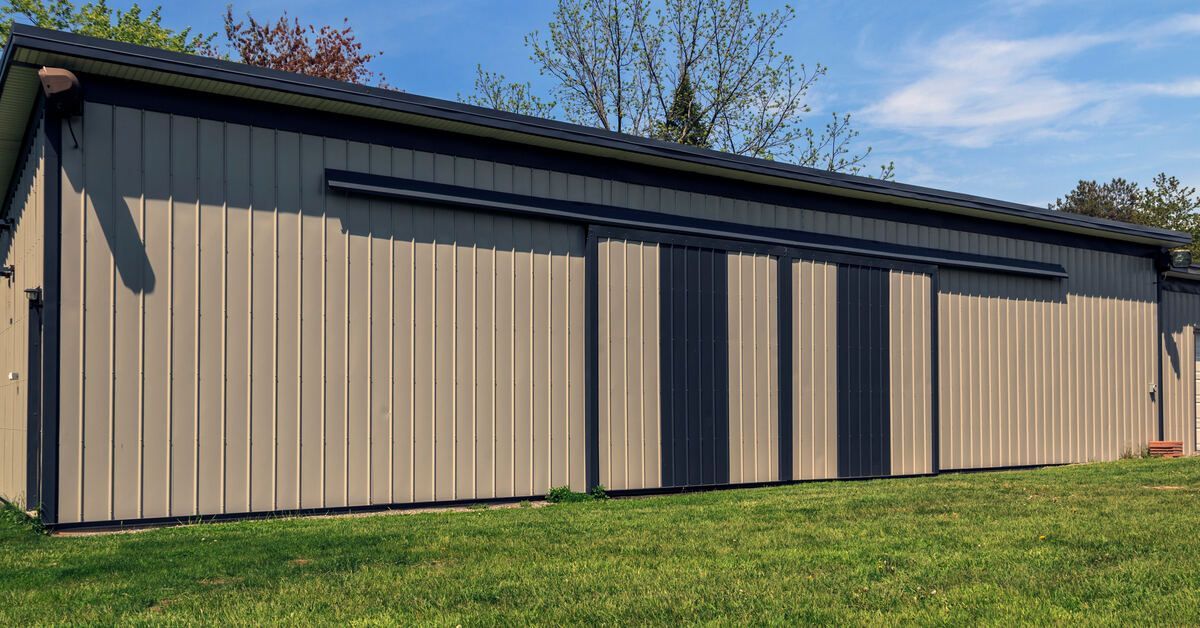 The exterior of a brown metal barn on a sunny day. The barn has a white garage door on one side of the building.