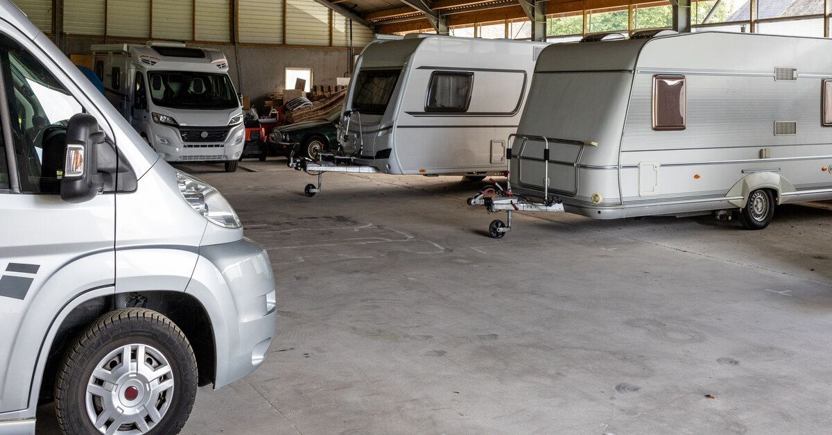 Several silver RVs and caravans parked inside a large structure with a concrete floor and a peaked roof.