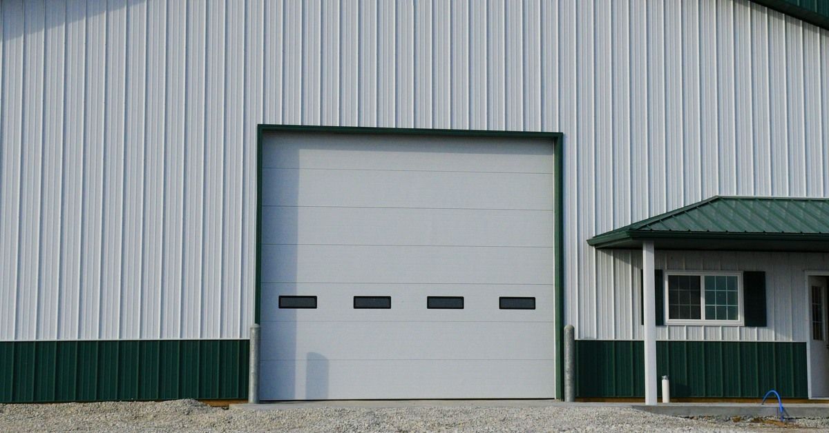 The exterior of a green and white barn with a peaked roof. There is a large door in the center of the building.