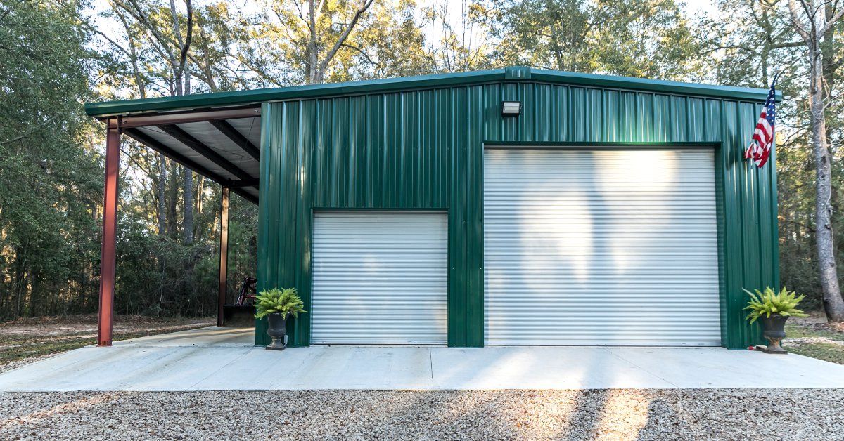 A large green metal building with two white roll-up doors and an American flag hanging from a pole on the front.