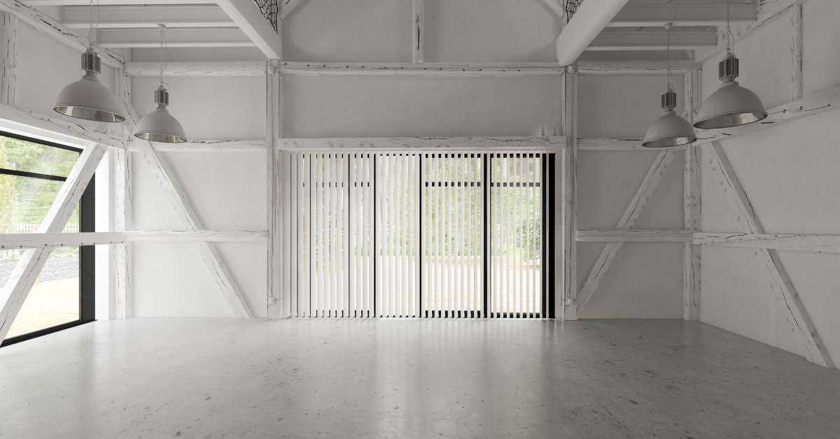 The interior of a barn home is painted in all white. Industrial lamps hang from beams across the ceiling.
