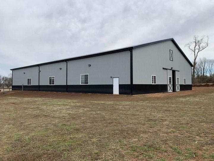 A large, rectangular metal barn with light gray upper walls and black lower walls, featuring sliding doors and windows.