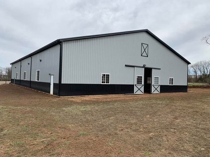 A grey and black metal barn with white-framed windows, a sliding entrance door, and an X-design on a grassy lot.